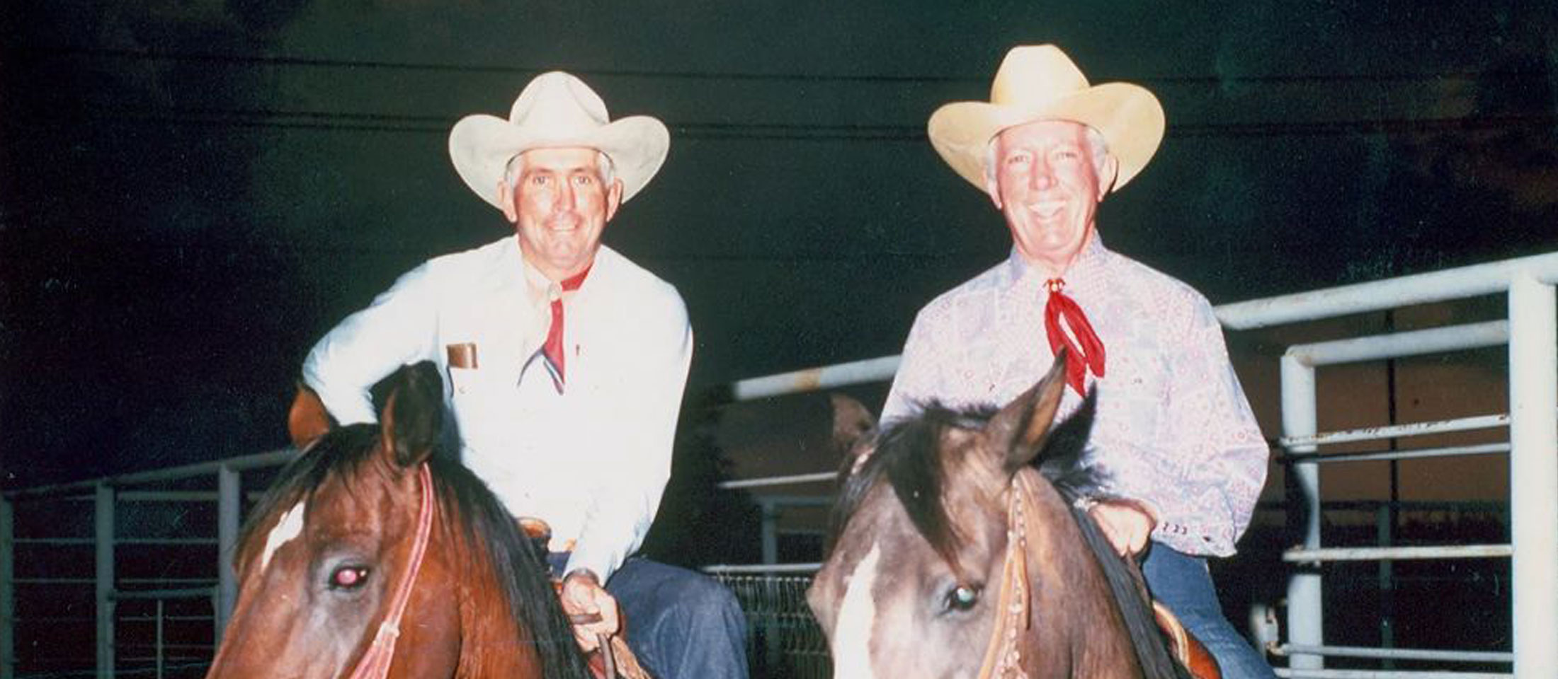 Older photo of two cowboys on horses in the evening.